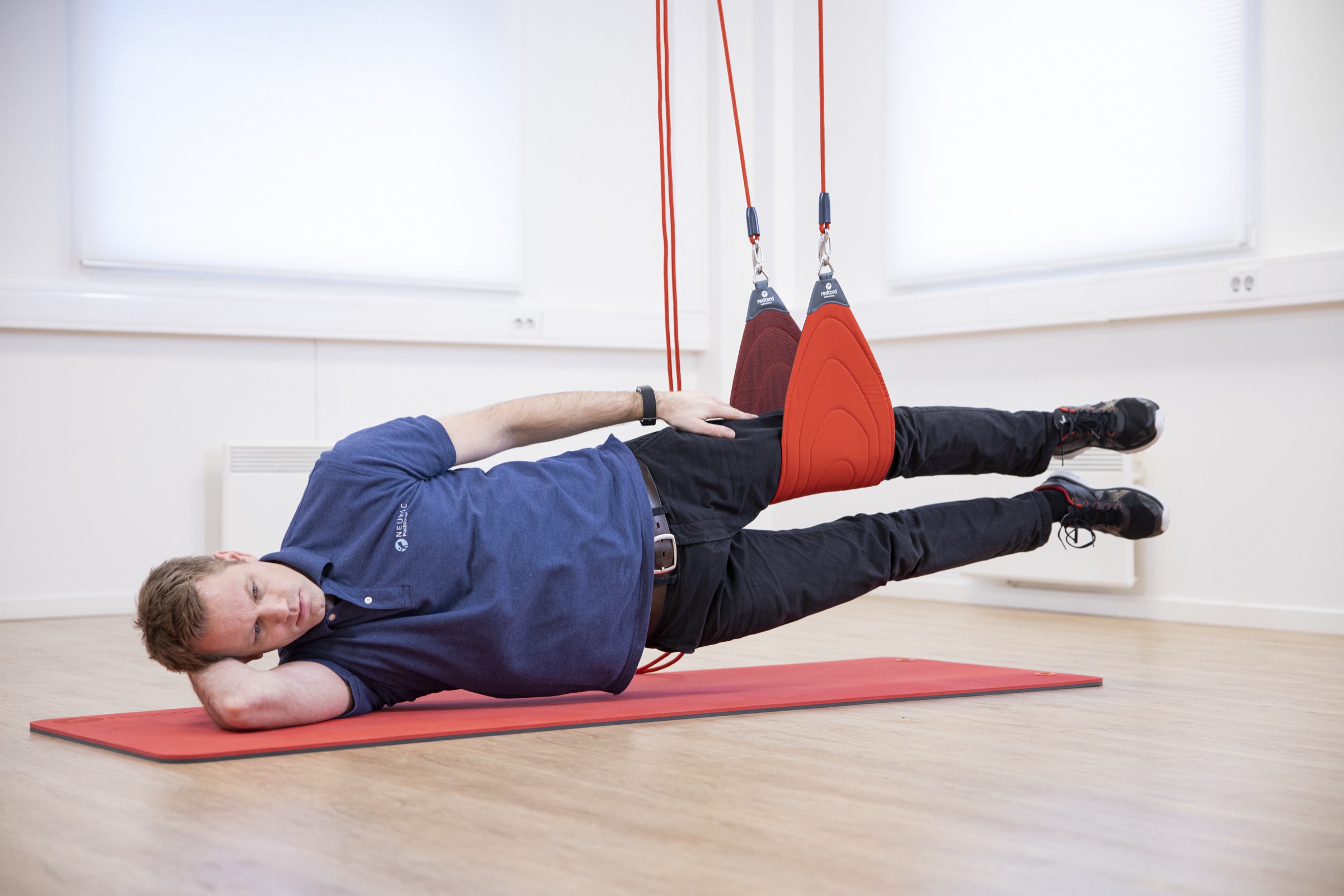 A participant holding a side-plank position with the hips supported in wide Redcord slings